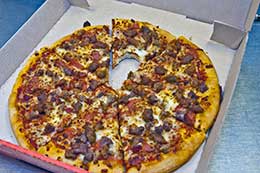 Pizza in box with a bite missing from a slice.